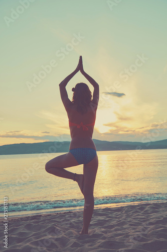 Young woman practicing yoga on the sandy beach.