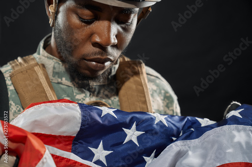Soldier in helmet sadly looking at national flag.