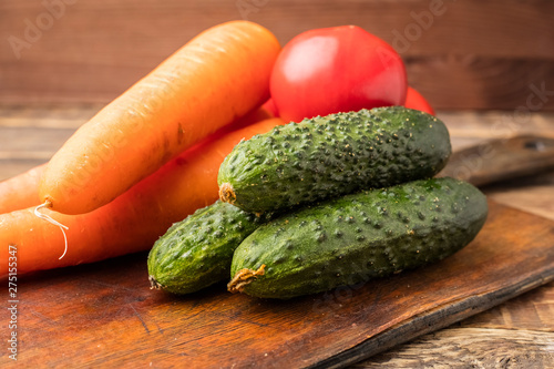 Ripe vegetables on an old wooden cutting board. Fresh crop of cucumbers, carrots, tomatoes. Salad preparation. Copy space