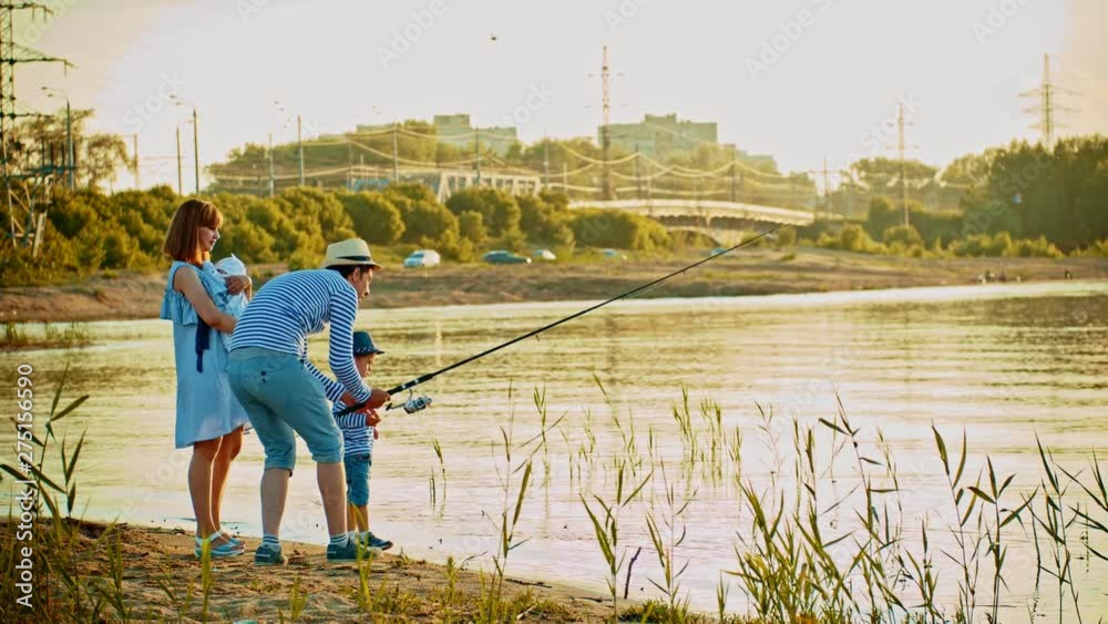 Family on fishing - father holding a fishing rod and showing his little son how to do it Family on fishing - father holding a fishing rod and showing his little son how to do it