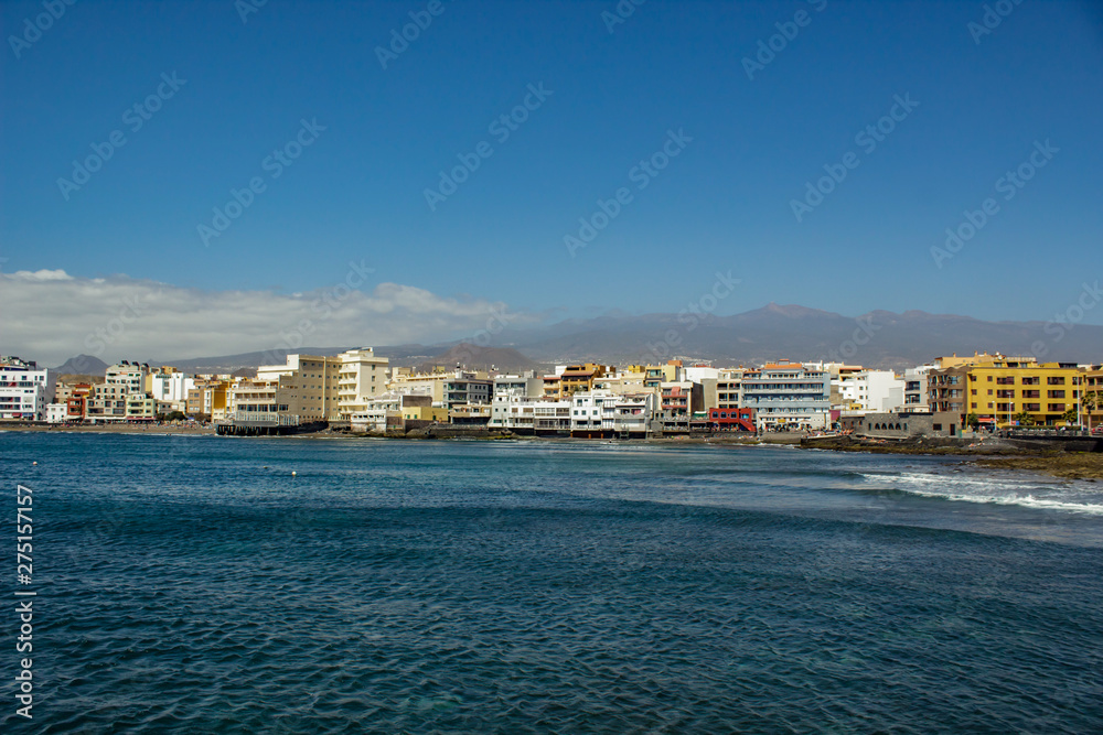 Wide angle panorama View of the volcanic beach towards the resort hotels, restaurants and terraces, in the bohemian village of El Medano in Granadilla de Abona, Tenerife.