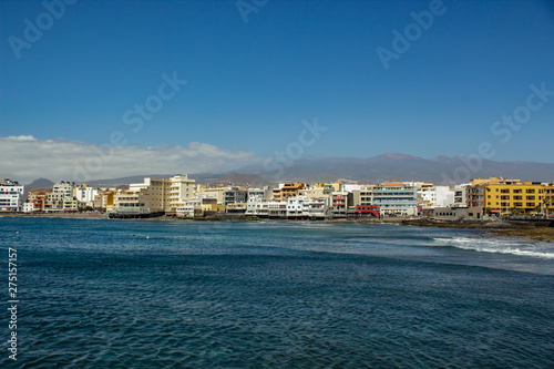 Wide angle panorama View of the volcanic beach towards the resort hotels, restaurants and terraces, in the bohemian village of El Medano in Granadilla de Abona, Tenerife.