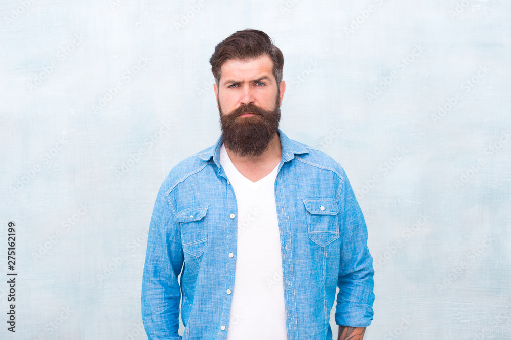 Bearded man trendy hipster style. Masculinity and male beauty concept. Hipster with beard and mustache wear denim shirt. Well groomed macho. Brutal handsome hipster man on grey wall background Bearded man trendy hipster style. Masculinity and male beauty concept. Hipster with beard and mustache wear denim shirt. Well groomed macho. Brutal handsome hipster man on grey wall background