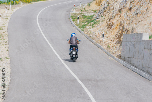 Biker wearing a waistcoat is riding his motorbike uphill on a sunny day.