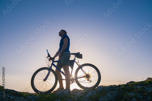 Strong fit male mountain biker performing stunts on rocky terrain on a sunset while wearing a blue shirt and riding a blue bike © qunica.com