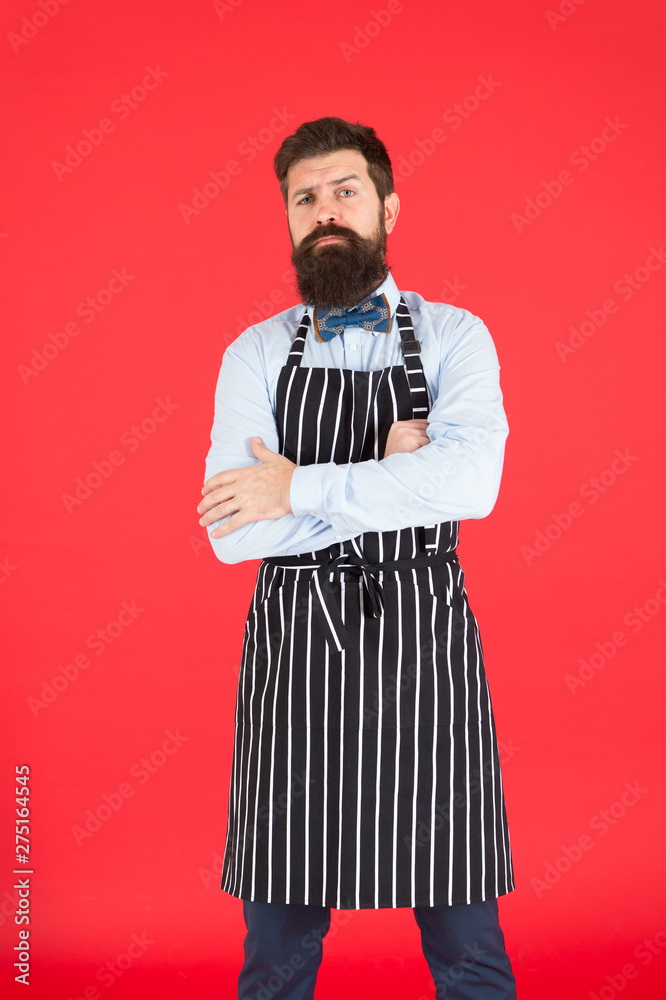 How can I help you. Hipster cafe concept. Man with beard cook hipster apron. Hipster chef cook red background. Bearded man chef cooking. Restaurant staff and service. Well groomed waiter at work