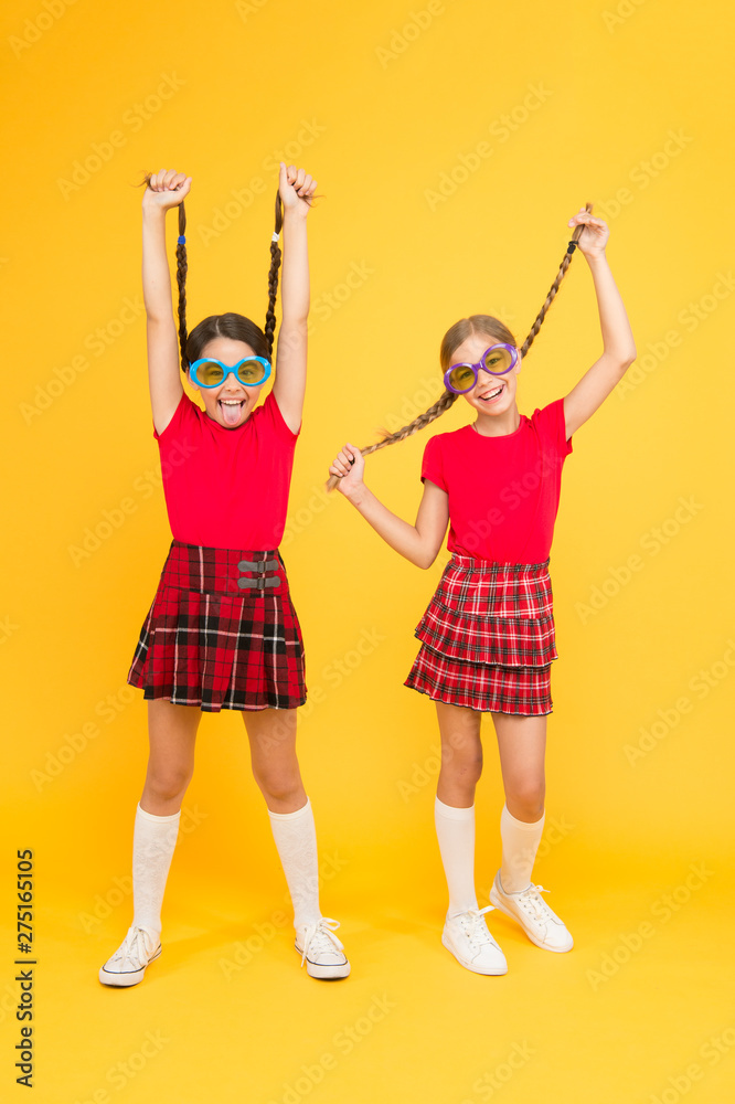Fototapeta premium Summer fashion trend. Kids fashionable friends posing in sunglasses on yellow background. Summer fun. Summer accessory. Girls cute sisters similar outfits wear colorful sunglasses for summer season