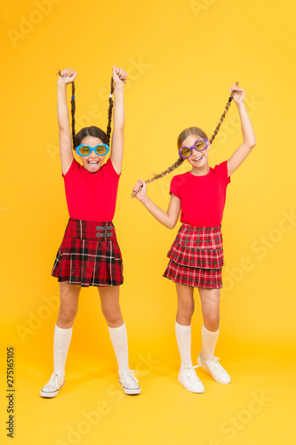 Summer fashion trend. Kids fashionable friends posing in sunglasses on yellow background. Summer fun. Summer accessory. Girls cute sisters similar outfits wear colorful sunglasses for summer season