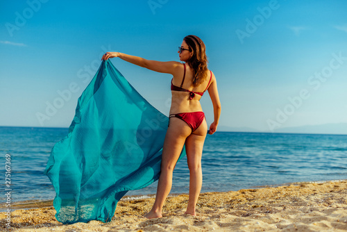 Young woman wearing bikini holding blue scarf on sand beach