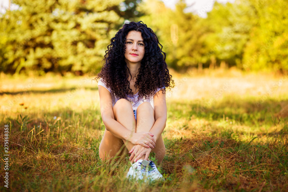 Pretty curly woman posing on grass in sunny day Pretty curly woman posing on grass in sunny day