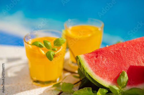 Summer holiday tropical concept. Fresh orange juice and watermelon juice and pineapple on border of a swimming pool.