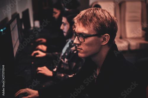 Portrait of blond young man in glasses at internet club playing videogames. photo