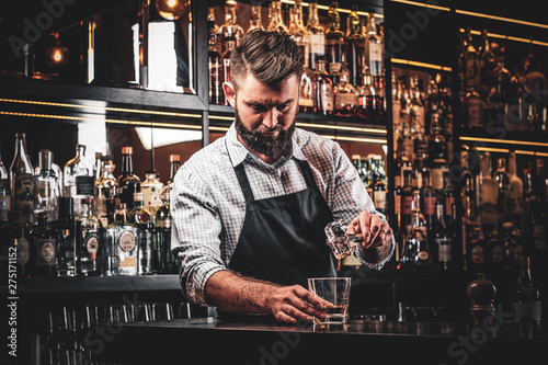 Diligent serious barman is preparing alcoholic beverege for customer. photo
