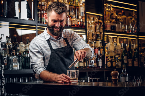 Happy smiling barman is prepairing drinks for customers at posh bar.