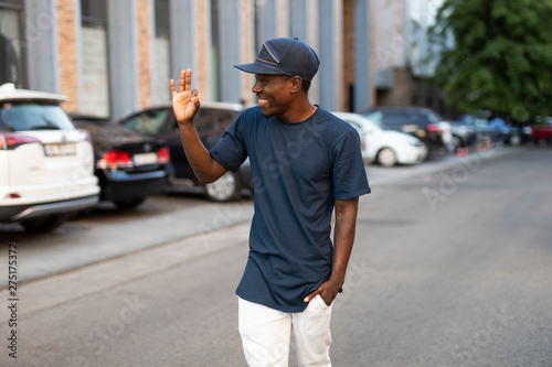 Happy african american man greets a friend waving his hand walking in city street, he glad to see you