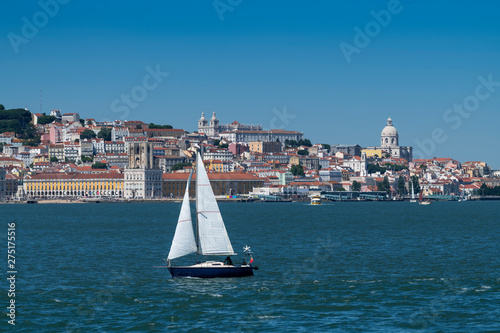 Small sailing boat in the Tagus River with the Lisbon skyline on the backround; Concept for travel in Portugal and visit Lisbon.