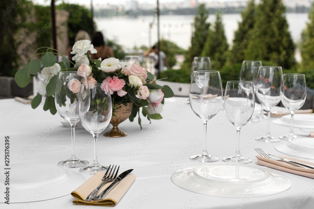 Wedding table setting decorated with fresh flowers in a brass vase. Wedding floristry. Banquet table for guests outdoors with a view of green nature. Bouquet with roses, eustoma and eucalyptus leaves