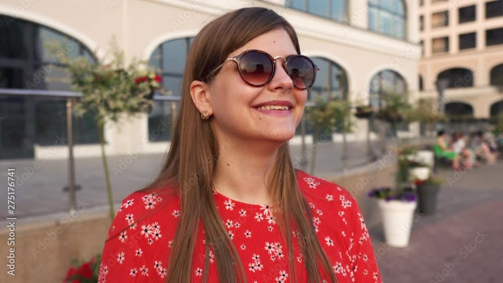 Close up portrait beautiful young woman looking at the sun and shaking his head. A girl in sunglasses and a red dress. Sunny summer and urban background. Concept happiness Close up portrait beautiful young woman looking at the sun and shaking his head. A girl in sunglasses and a red dress. Sunny summer and urban background. Concept happiness