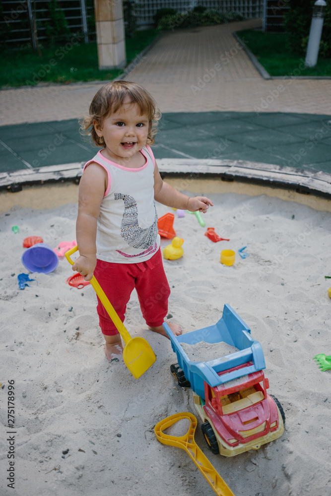 Fototapeta premium Baby girl in sandbox playing with toys