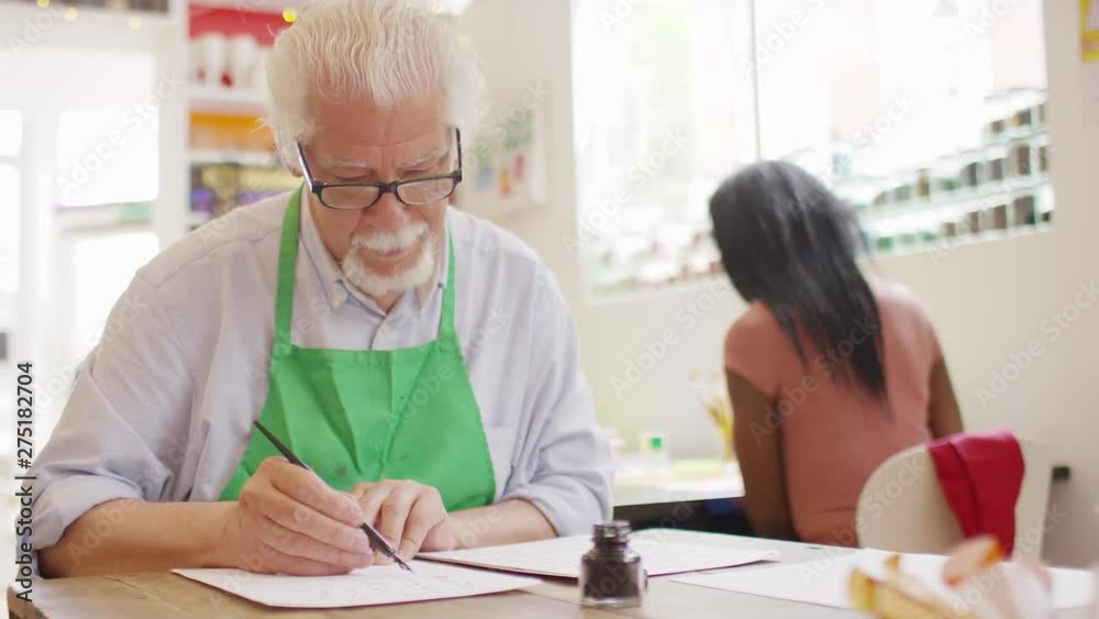 Portrait of senior man in an art class smiling to camera as he learns calligraphy Portrait of senior man in an art class smiling to camera as he learns calligraphy