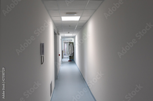 Lab jackets are seen blurred in the background of a long passageway inside a technology and research facility. Long white walls lead down a futuristic building.