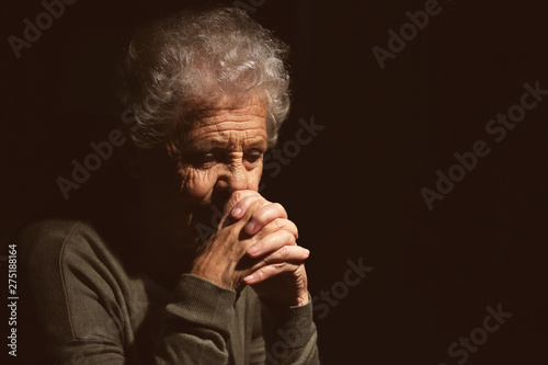 Senior woman praying to God on dark background