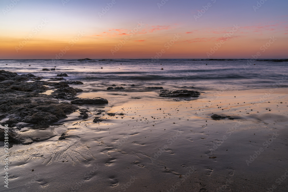 Dusk over the ocean with orange and purple sky reflecting on the beach