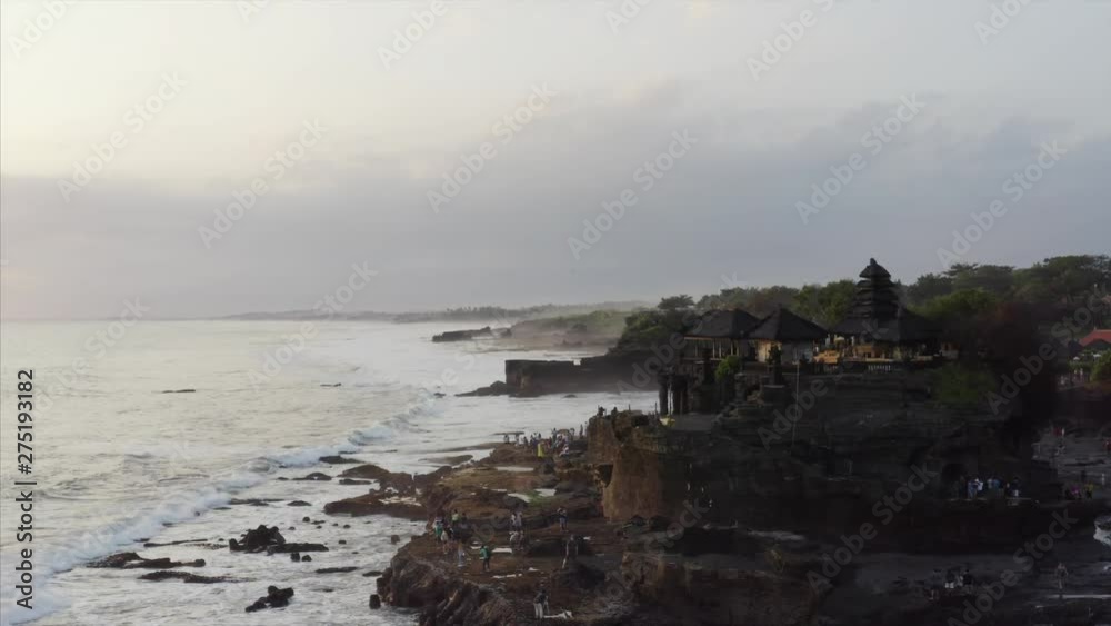Beautiful aerial zooming out view of Hindu pilgrimage temple Pura Tanah Lot and tourists visiting it. It's a popular tourist and cultural icon for photography. Bali, Indonesia Beautiful aerial zooming out view of Hindu pilgrimage temple Pura Tanah Lot and tourists visiting it. It's a popular tourist and cultural icon for photography. Bali, Indonesia