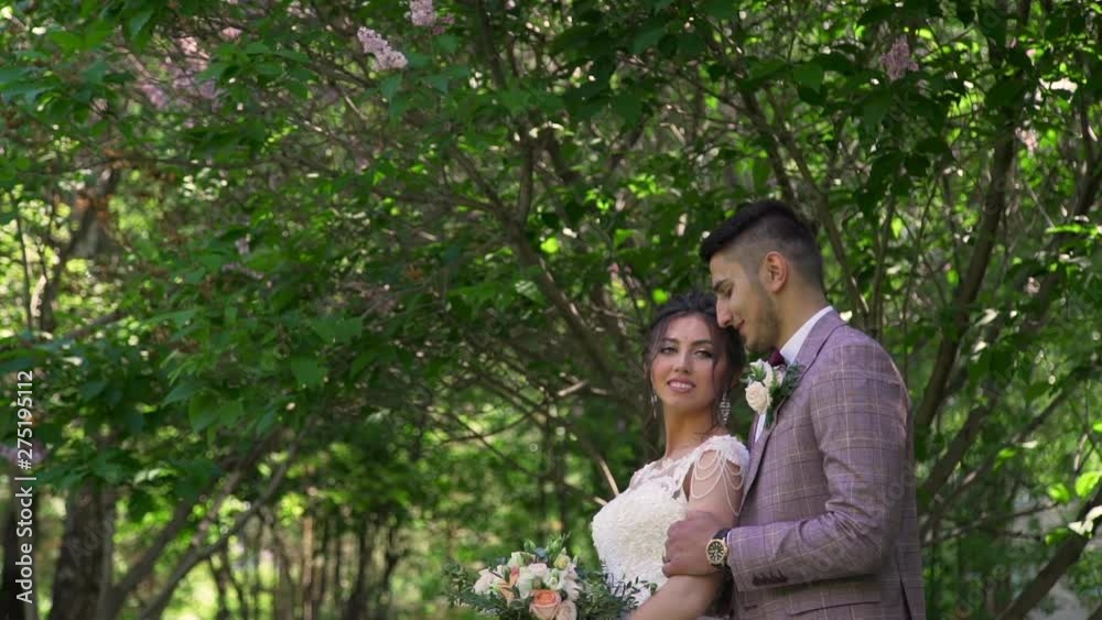 Lovely Bride and Groom Hugging and Smiling in the City Park in Summer Day. Slow Motion. Happy Marriage and Wedding Day Concept Lovely Bride and Groom Hugging and Smiling in the City Park in Summer Day. Slow Motion. Happy Marriage and Wedding Day Concept