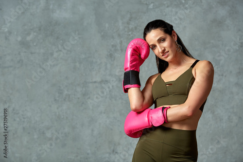 Beautiful athletic girl posing in pink boxing gloves on a gray background. Copy space. Concept sport, fight, goal achievement. © Georgii