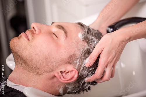 Master washes the head of the client in the Barber shop, hairdresser makes hairstyle for a young man.