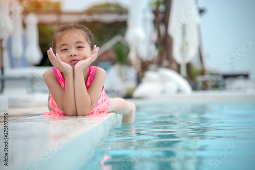 Cheerful cute girl at swimming pool on summer vacation with happiness smiling face. Smile adorable little toddler have fun with pink swimming suit in sunshine day. funny girl and smile kid concept. © aFotostock