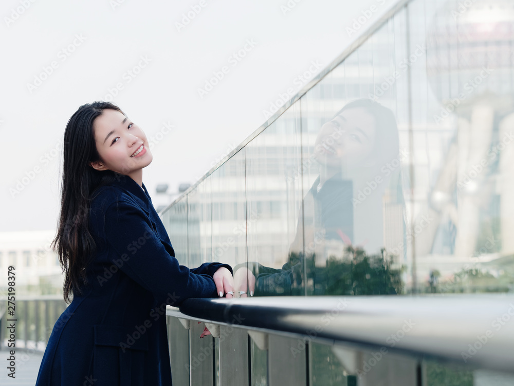 Beautiful Chinese girl with her mirror image in glass, portrait of young Asian woman with black long hair, smiling and happy.
