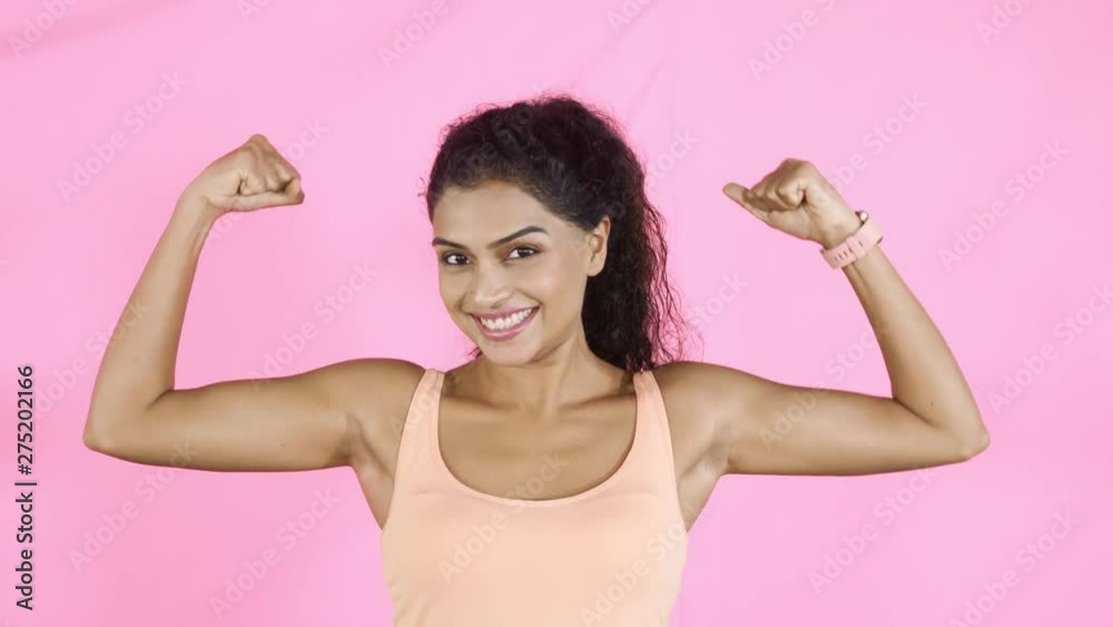 Healthy woman showing her muscle while smiling at the camera in the studio. Shot in 4k resolution Healthy woman showing her muscle while smiling at the camera in the studio. Shot in 4k resolution