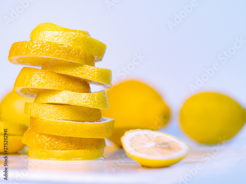 Several lemons and pile of slices on light background, close up view. Set of yellow lemons on desk, freshly cutted fruits composition. Blurred background. Selective soft focus