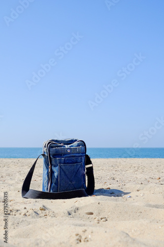 Close-up of blue denim bag with black strap on sandy beach against blue sky