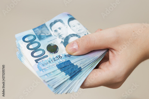 Hand holding folded bundle of blue money in cash of one thousand Philippines peso. Giving bribe, paying bills or getting salary. Payment day!