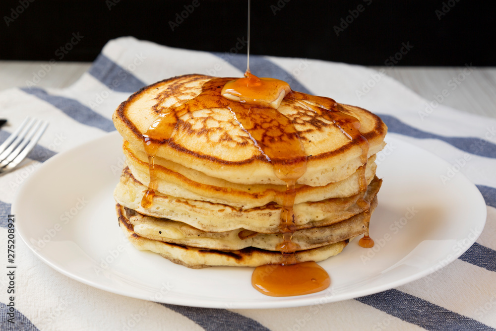 Homemade pancakes with butter and maple syrup on a white plate, side view. Closeup.