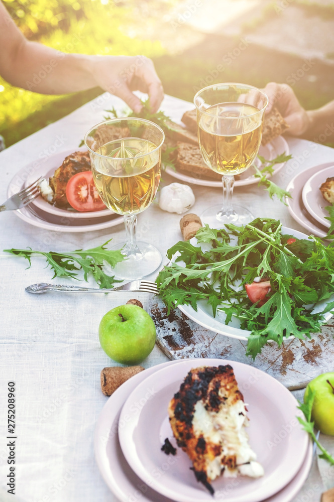 People eat at the table in the garden. Dinner at sunset with wine, grilled fish, fresh vegetables and herbs. Vertical shot People eat at the table in the garden. Dinner at sunset with wine, grilled fish, fresh vegetables and herbs. Vertical shot
