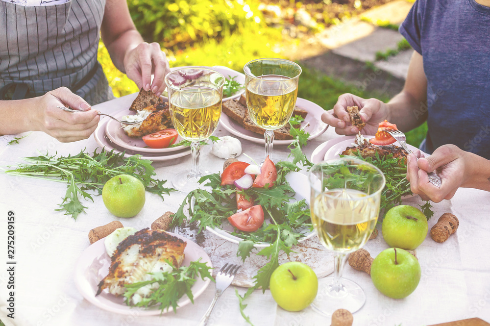 Dinner in the garden. People eat at the table with wine, grilled fish, fresh vegetables and herbs. Horizontal shot Dinner in the garden. People eat at the table with wine, grilled fish, fresh vegetables and herbs. Horizontal shot