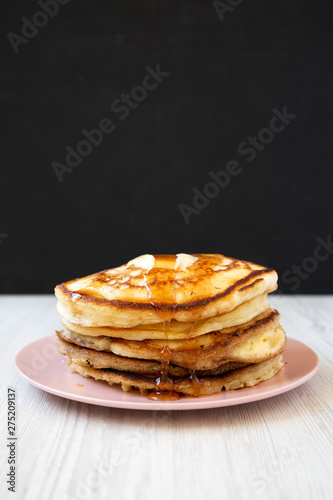 Homemade pancakes with butter and maple syrup on a pink plate, side view. Close-up.