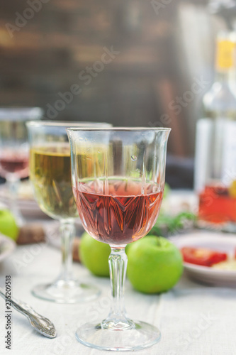 Glasses of white and rose wine, grilled fish plates, vegetables, salad and fruits on the table. Summer party in the backyard. Vertical shot