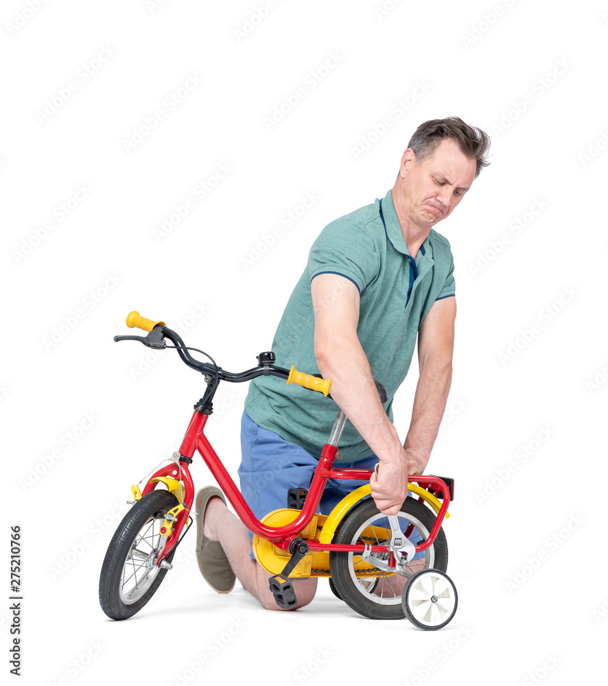 Obraz premium Man in shorts and a t-shirt is repairing a children's bicycle, in the hands of a wrench. Isolated on white background.
