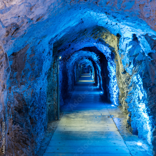 tight and narrow old tunnel leading through a mountain with blue lighting to guide the way