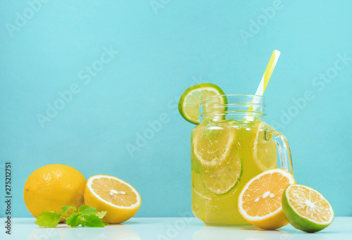Lemonade drink of soda water, citrus and mint on the light blue background. Cocktail glass with handle and straw, sliced lemon and lime, front view