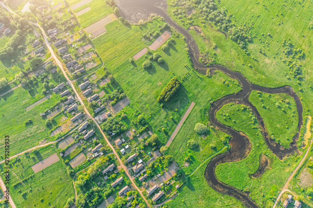 Fototapeta premium Aerial view from the height of the village with houses and streets, plowed fields, meadows, river in the summer.