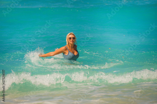 young happy and sexy blond woman in bikini playing with waves in the sea at stunning beautiful tropical beach enjoying carefree summer holidays in travel concept