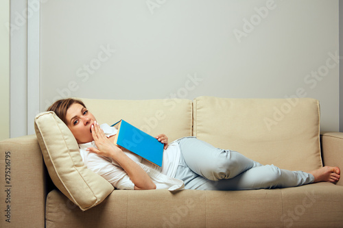 Yawning woman lying on sofa with open book