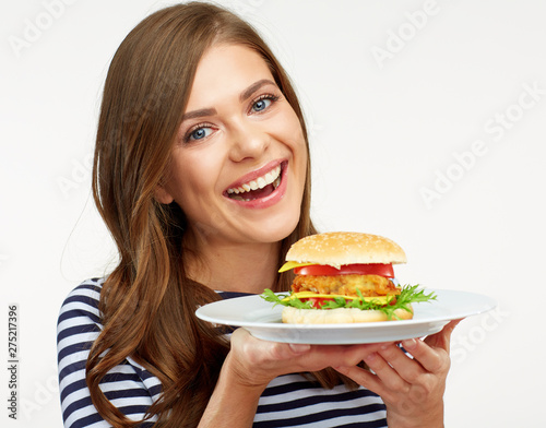 Smiling woman holding burger on white plate.