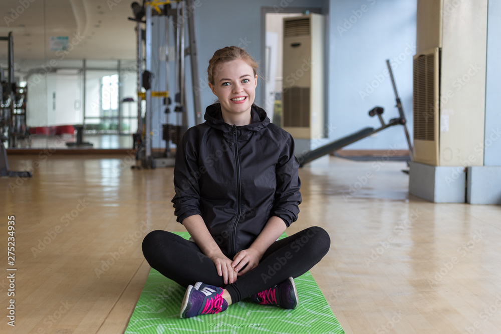 Young caucasian woman sitting on a mat at the gym smiling Young caucasian woman sitting on a mat at the gym smiling